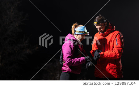 Checking Coordinates During Night Hike.Couple night hikers examine a device under headlamp light, emphasizing navigation and teamwork under low light conditions. 129887104