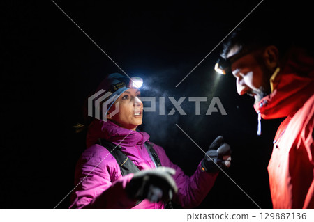 Nighttime First Aid in the Wilderness.A woman provides headlamp-assisted first aid to a man outdoors in the dark, showcasing emergency preparedness in extreme conditions. 129887136