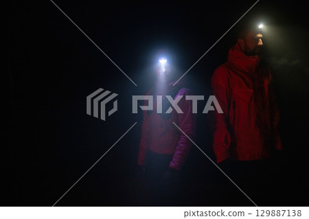 Exploring the Night Forest.Couple equipped with headlamps explore a forest in total darkness, with beams of light cutting through the night air. Exploring the Night Forest.Couple equipped with headlamps explore a forest in total darkness, with beams of light cutting through the night air. 129887138