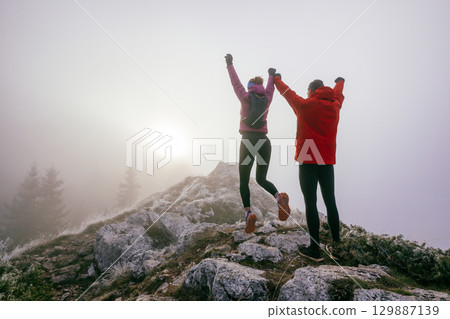 Two Hikers Celebrating on Rocky Peak.Couple hikers raising fists on rugged mountain ridge at sunrise. 129887139