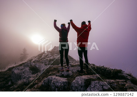 Two Hikers Celebrating on Rocky Peak.Couple hikers raising fists on rugged mountain ridge at sunrise. Two Hikers Celebrating on Rocky Peak.Couple hikers raising fists on rugged mountain ridge at sunrise. 129887142