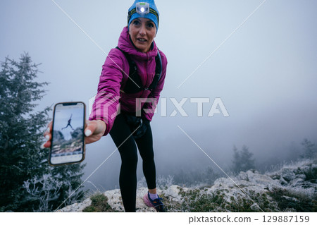 Female Hiker Showing Smartphone Photo.Female hiker displaying a smartphone image on a mountain covered in early fog. Female Hiker Showing Smartphone Photo.Female hiker displaying a smartphone image on a mountain covered in early fog. 129887159