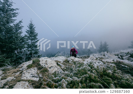 Female Trail Runner in Motion.Back view of female trail runner in pink jacket and black leggings running uphill. 129887160