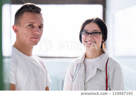 Male and female medical professionals smiling and standing together in a hospital hallway. Concept of teamwork and care. Male and female medical professionals smiling and standing together in a hospital hallway. Concept of teamwork and care. 129887193
