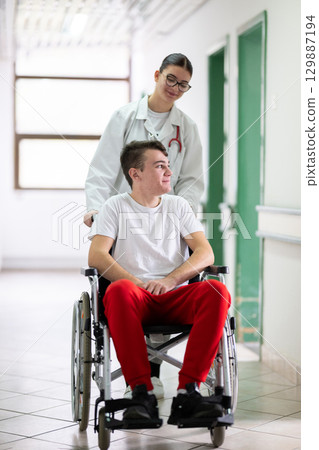 Young Male Patient in Wheelchair Assisted by Female Medical Professional Young Male Patient in Wheelchair Assisted by Female Medical Professional 129887194