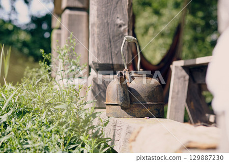 Rusty kettle resting on a wooden table surrounded by green plants in a peaceful outdoor setting 129887230