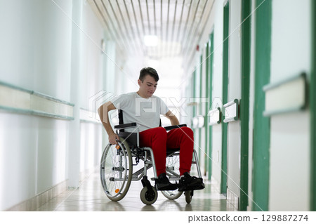Young teenage boy smiling while sitting in a wheelchair in a hospital hallway. Rehabilitation and positivity concept. Young teenage boy smiling while sitting in a wheelchair in a hospital hallway. Rehabilitation and positivity concept. 129887274