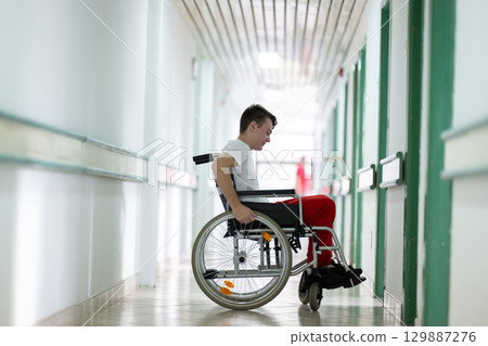 Young teenage boy smiling while sitting in a wheelchair in a hospital hallway. Rehabilitation and positivity concept. 129887276