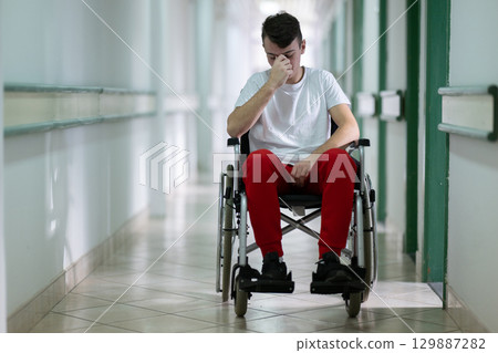 Sad Young Man in Wheelchair.Teenage boy sitting in wheelchair with sad expression in hospital hallway. Emotion and struggle in recovery. Sad Young Man in Wheelchair.Teenage boy sitting in wheelchair with sad expression in hospital hallway. Emotion and struggle in recovery. 129887282