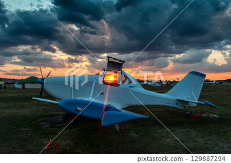 White agricultural private airplane with open cockpit against the backdrop of a scenic sunrise 129887294