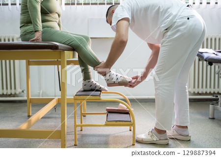Physical Therapist Assisting Elderly Patient.Physiotherapist helping an elderly woman with leg movement on a step platform during a rehabilitation session. 129887394