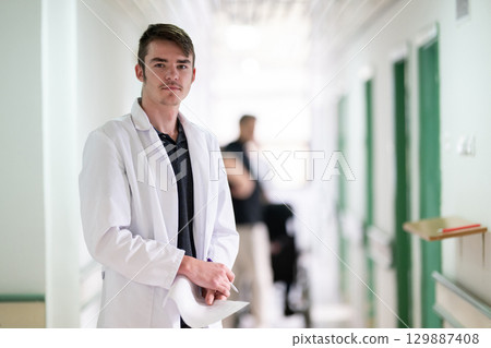 Doctor Reading Documents in Hospital.Young male doctor walking in hospital hallway while reading patient documentation. Clinical work environment. 129887408