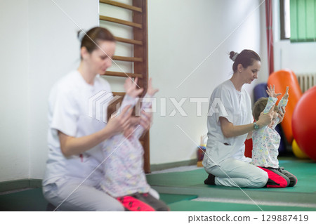 Pediatric Physiotherapy Session.Female physiotherapist helping a young child with physical exercises in a rehabilitation center. Pediatric therapy and development concept. 129887419