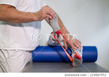 Leg Resistance Band Therapy.Therapist assisting with leg stretching using a resistance band during physical rehabilitation therapy session. 129887452