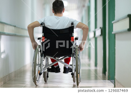 Young teenage boy smiling while sitting in a wheelchair in a hospital hallway. Rehabilitation and positivity concept. 129887469