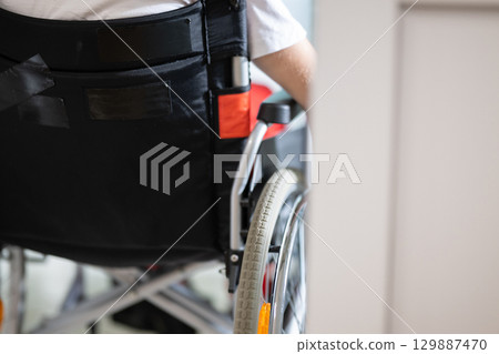 Young teenage boy smiling while sitting in a wheelchair in a hospital hallway. Rehabilitation and positivity concept. 129887470
