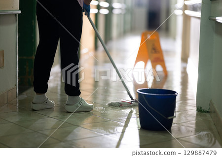 Cleaning Staff in Hospital Hallway.Female janitor standing in a hospital corridor with mop and bucket, symbolizing cleanliness and hygiene. 129887479