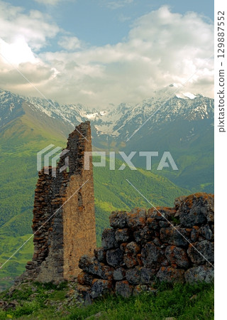 Ancient architecture and ruins against mountain background . Remains of a destroyed tower . North Ossetia-Alania , Russia Ancient architecture and ruins against mountain background . Remains of a destroyed tower . North Ossetia-Alania , Russia 129887552