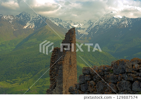 Ancient architecture and ruins against mountain background . Remains of a destroyed tower . North Ossetia-Alania , Russia Ancient architecture and ruins against mountain background . Remains of a destroyed tower . North Ossetia-Alania , Russia 129887574