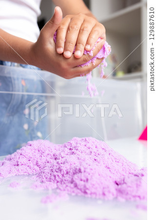 Child playing with purple kinetic sand indoors for creative fun 129887610