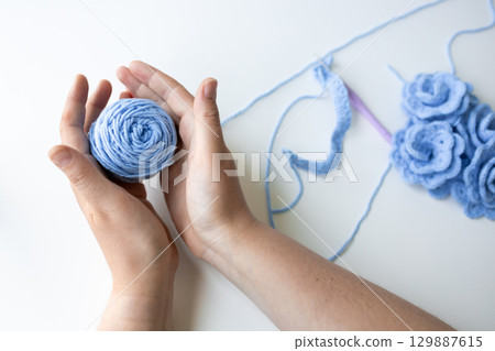 Caucasian female hands holding blue yarn ball for crochet crafting on white background 129887615