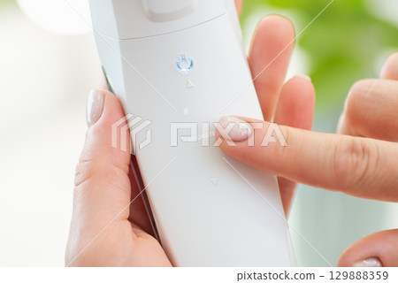 Close up of white ultrasonic skin scrubber in female hand. Finger pointing on the word "hydrate" on cosmetic device Close up of white ultrasonic skin scrubber in female hand. Finger pointing on the word "hydrate" on cosmetic device 129888359