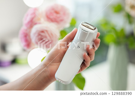Tool for facial massage in hand of a professional cosmetologist, close up, flowers on the background. Professional device for body and skin care concept Tool for facial massage in hand of a professional cosmetologist, close up, flowers on the background. Professional device for body and skin care concept 129888390