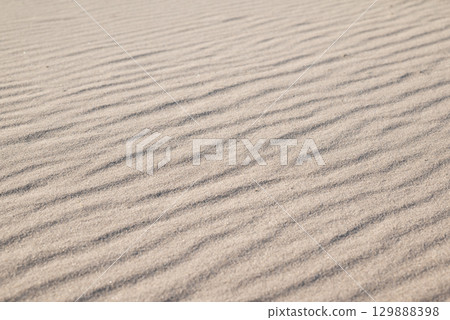 Sand beach with waves. Close up of sand under bright sunlight, wind made waves on it 129888398