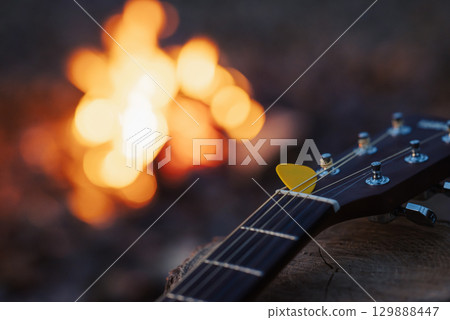 Close up on yellow mediator on guitar with bonfire on the background. Playing guitar, music, having good time camping on nature Close up on yellow mediator on guitar with bonfire on the background. Playing guitar, music, having good time camping on nature 129888447