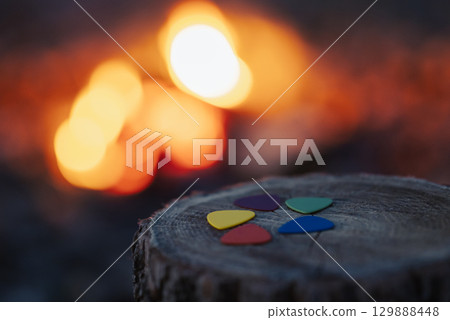 Evening shot of colorful mediators on stump. Camping on nature, mediators for playing guitar Evening shot of colorful mediators on stump. Camping on nature, mediators for playing guitar 129888448