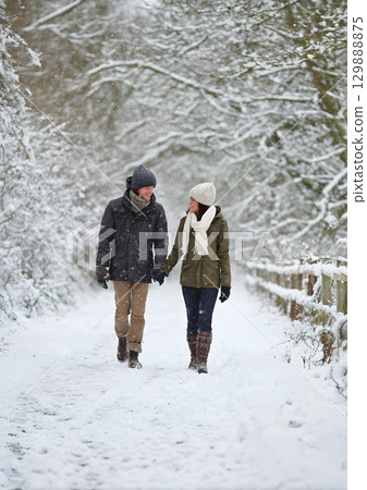 couple walking hand in hand through snowy path couple walking hand in hand through snowy path 129888875
