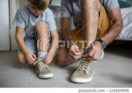 dad tying shoelaces for boy preparing for school morning 129889908