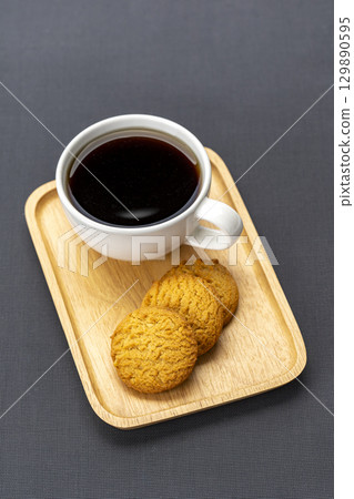Black coffee with three cookies on wooden tray, minimal style, on dark background, warm and inviting, perfect for breakfast or snack, simple and cozy presentation 129890595