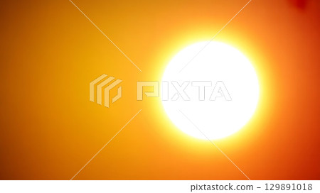 Bright glowing sun with halo effect against gradient orange background capturing radiant solar energy 129891018