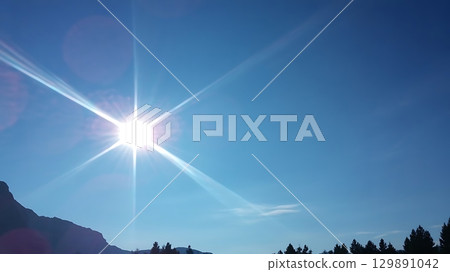 Sun flare in blue sky above mountain and tree silhouettes on sunny day 129891042