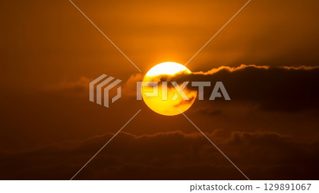 Sun flare above horizon with clouds and red-orange sky creating bold contrast and glowing atmospheric effect 129891067