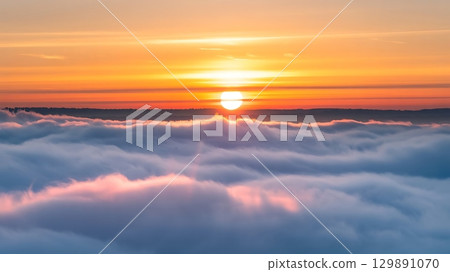 Sunrise over a sea of clouds with an orange sky and a distant horizon Sunrise over a sea of clouds with an orange sky and a distant horizon 129891070