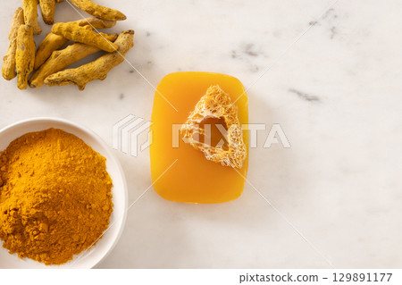 Turmeric soap bar and powder turmeric root on marble white background. Organic skincare product perfect for wellness, beauty, and organic body care concepts. View from above. 129891177