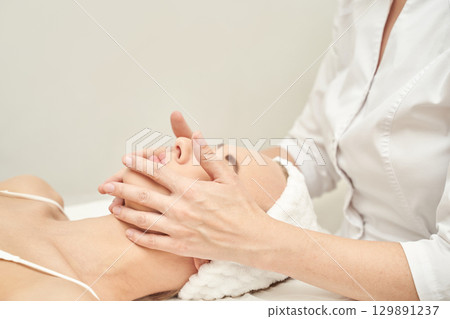 Caucasian young female relaxing during professional facial massage at spa 129891237