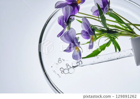 A drop of serum and a pipette with pansies in close-up. A drop of serum and a pipette with pansies in close-up. 129891262