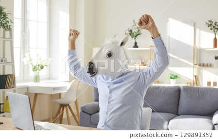 Funny extravagant happy man wearing donkey, horse head happy celebrating near laptop online 129891352