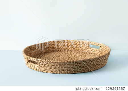 Round woven wicker basket, tray or plate stand on blue background. Handmade by local craftsmen in sri lanka traditional tableware. Round woven wicker basket, tray or plate stand on blue background. Handmade by local craftsmen in sri lanka traditional tableware. 129891367