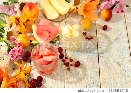 Autumn-summer banner with fruit drinks. Still life with flowers, lilies, mint, mallow, daisies, apples, melons, cherries and watermelon on a sunny table. Abstract floral composition, background, Autumn-summer banner with fruit drinks. Still life with flowers, lilies, mint, mallow, daisies, apples, melons, cherries and watermelon on a sunny table. Abstract floral composition, background, 129891748