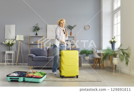 Smiling woman dancing in living room with suitcases around, celebrating and preparing for vacation. 129891811