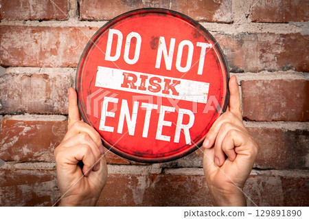 Red Circular Warning Sign with Text Do Not Risk Enter Held Against Brick Wall 129891890