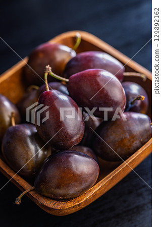 Ripe plums in bowl on black table. 129892162