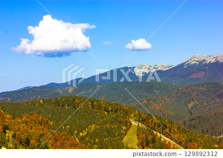 Autumn forest with a ski slope cutting through it and mountains. A stunning autumnal landscape showcasing a vibrant forest with a ski slope cutting through the trees and mountains in the background. Autumn forest with a ski slope cutting through it and mountains. A stunning autumnal landscape showcasing a vibrant forest with a ski slope cutting through the trees and mountains in the background. 129892312