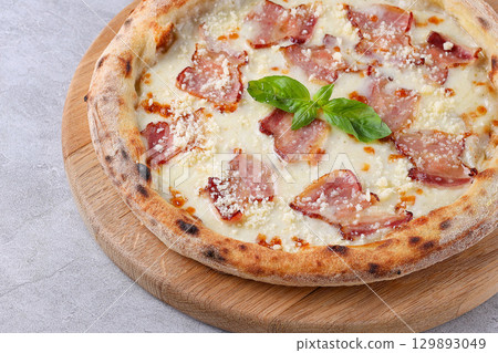 White sauce pizza topped with crispy bacon, grated cheese, and fresh basil, served on a wooden board. White sauce pizza topped with crispy bacon, grated cheese, and fresh basil, served on a wooden board. 129893049