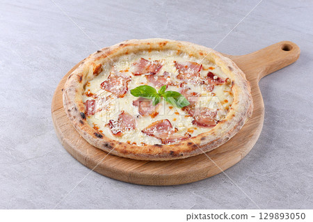 White sauce pizza topped with crispy bacon, grated cheese, and fresh basil, served on a wooden board. White sauce pizza topped with crispy bacon, grated cheese, and fresh basil, served on a wooden board. 129893050