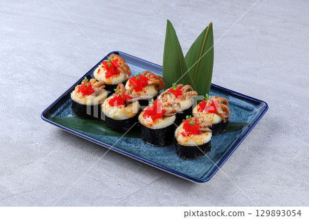 Elegant sushi platter with octopus, fish roe, and herbs on seaweed-wrapped rice, served on a blue ceramic plate with green leaves Elegant sushi platter with octopus, fish roe, and herbs on seaweed-wrapped rice, served on a blue ceramic plate with green leaves 129893054